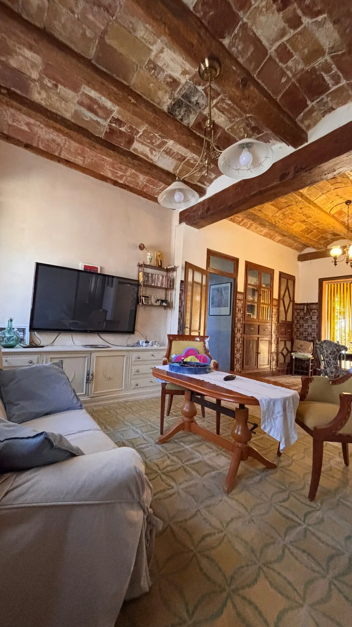 Salón con techo de bóveda catalana de ladrillo visto, vigas de madera, suelo hidráulico y televisión de gran formato
