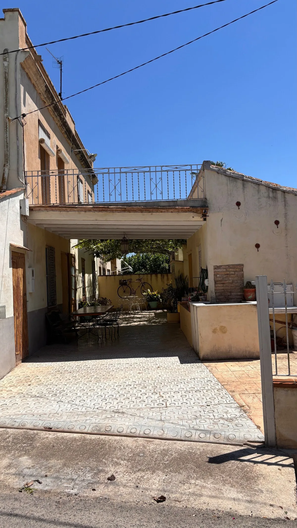 Entrada al porche desde la calle, con la terraza superior con barandilla de forja y la parra al fondo