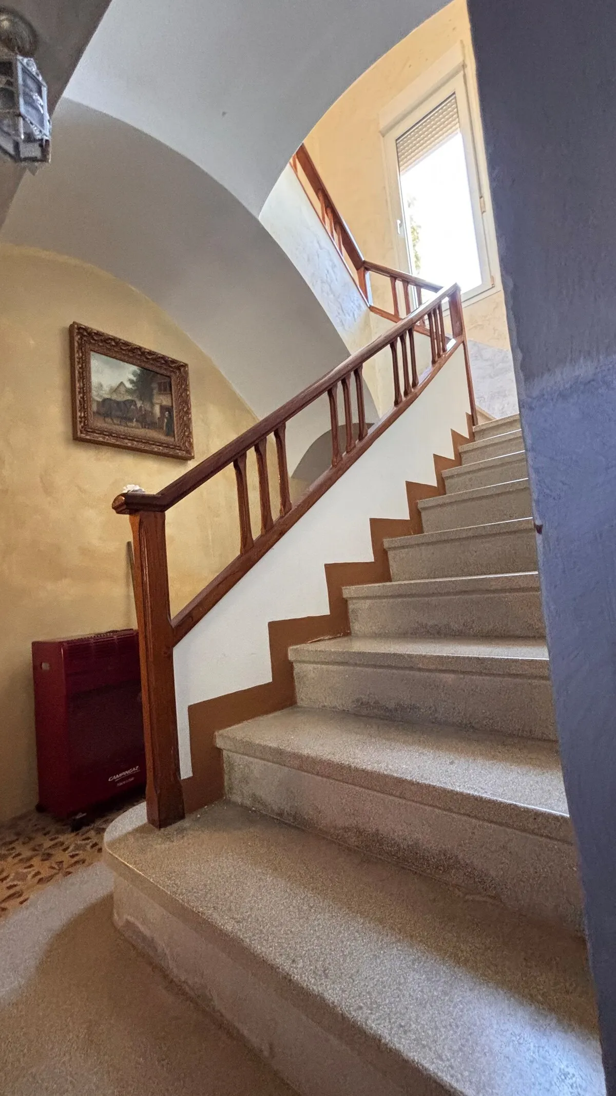 Escalera de la casa bajo una bóveda encalada, con barandilla de madera y paredes en tono ocre